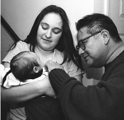 Social worker Jacob Ocampo  gently touching a new born infant, who is being held by the smiling mother.